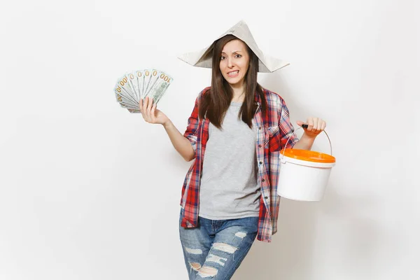 Betrokken vrouw in krant hoed bedrijf bundel van dollars, contant geld en lege emmertje met kopie ruimte geïsoleerd op een witte achtergrond. Instrumenten voor renovatie appartement. Reparatie home concept. — Stockfoto