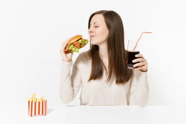 Jovem divertida sentada à mesa com hambúrguer, batatas fritas, cola em garrafa de vidro isolada no fundo branco. Nutrição adequada ou fast food clássico americano. Área de publicidade com espaço de cópia . — Fotografia de Stock