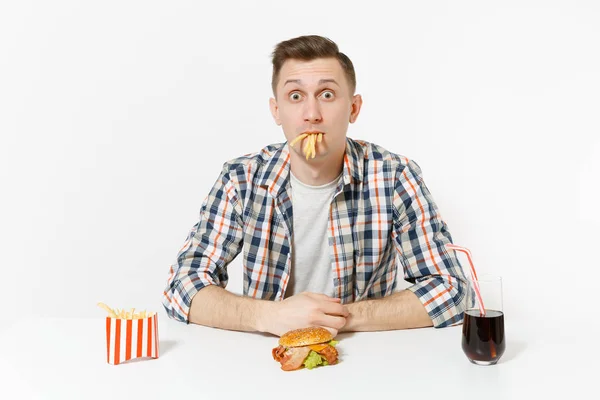 Patates kızartması yemek, burger tabloyla, cola cam beyaz arka plan üzerinde izole oturup eğlenceli aç genç adam. Doğru beslenme veya Amerikan Klasik fast food. Alan kopya alanı ile reklam. Telifsiz Stok Fotoğraflar