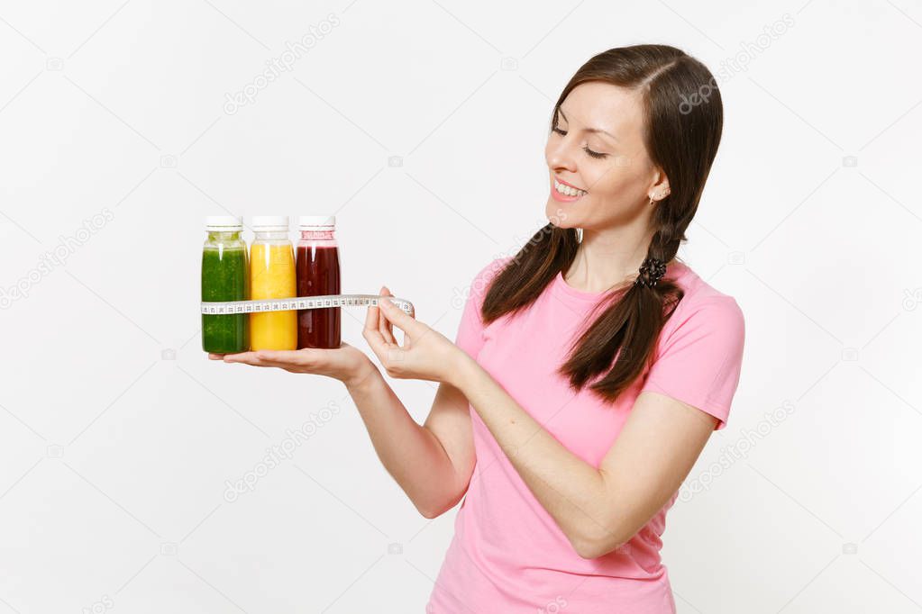 Woman holds row of green, red, yellow detox smoothies in bottles, measure tape isolated on white background. Proper nutrition, vegetarian drink, healthy lifestyle, dieting concept. Copy space, flack.