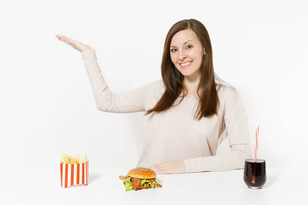 Giovane donna che punta mano da parte su spazio copia a tavola con hamburger, patatine fritte, cola in bottiglia di vetro isolata su fondo bianco. Una corretta alimentazione o un fast food classico americano. Area pubblicitaria . — Foto Stock