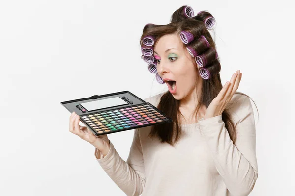 Fun young woman with curlers on hair with palette colorful eyeshadows isolated on white background. Makeup with set facial decorative cosmetics. Beauty fashion lifestyle concept. Area with copy space. — Stock Photo, Image