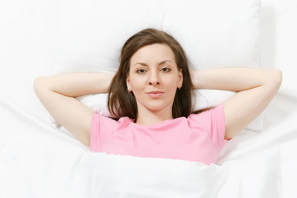 Top view of happy brunette young woman lying in bed with white sheet, pillow, blanket, hands under head. Smiling female spending time in room. Rest, relax, good mood concept. Copy space advertisement. — Stock Photo, Image