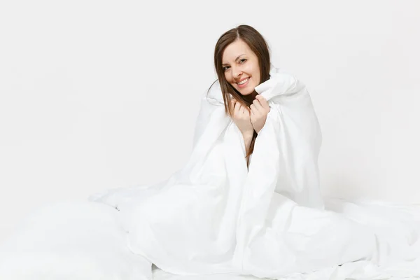 Ung brunett kvinna sitter i sängen med vitt lakan, kudde, inslagning i filt på vit bakgrund. Skönhet kvinna umgås i rummet. Vila, koppla av, gott humör koncept. Kopiera utrymme för reklam — Stockfoto