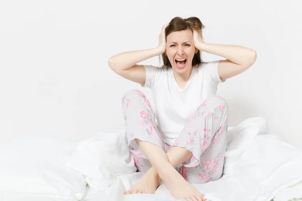 Stressed crazy mad young screaming woman sitting in bed with white sheet, pillow, blanket. Shocked female cover ears with hands, spending time in room. Bad mood, stress, problem concept. Copy space. — Stock Photo, Image