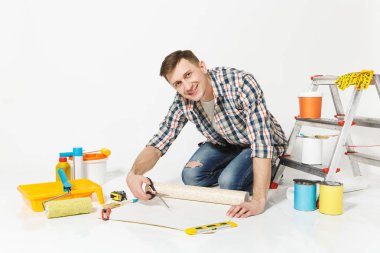 Duvar kağıdı rulo, makas, beyaz arka plan üzerinde izole yenileme daire oda için aygıtlar ile katta oturan genç adam. , Duvar kağıdı yapıştırma aksesuarları, boyama araçlarını. Onarım ev concept