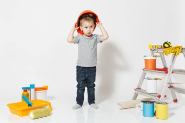 Beyaz arka plan üzerinde izole yenileme daire için aygıtlar ile turuncu koruyucu kask içinde küçük bir çocuk. , Duvar kağıdı yapıştırma aksesuarları, boyama araçlarını. Onarım ev. Ebeveynlik, çocukluk kavramı