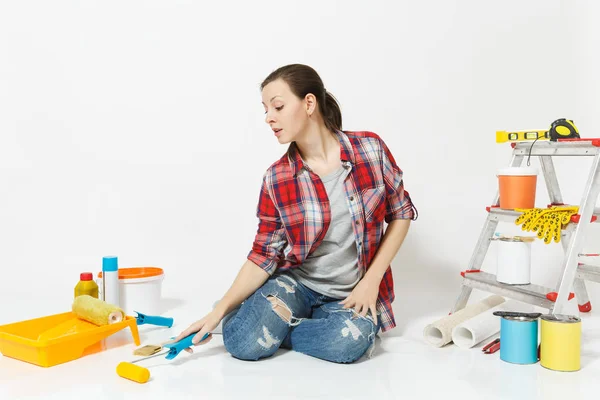 Woman in casual clothes sitting on floor with paint roller, instruments for renovation apartment isolated on white background. Wallpaper, accessories for gluing, painting tools. Repair home concept.