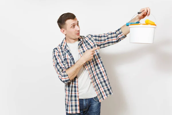 Young geschokt knappe man index vinger op lege emmertje met kopie ruimte en verf roller voor wandschildering geïsoleerd op een witte achtergrond. Renovatie appartement kamer. Reparatie home concept. — Stockfoto