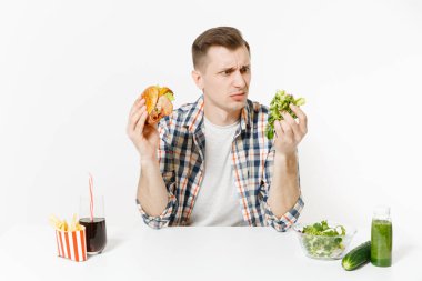 Adam masada yeşil Detoks smoothies, cam kase, salatalık, burger, patates, kola cam beyaz arka plan üzerinde izole salata ile oturuyor. Doğru beslenme, sağlıklı yaşam, lokanta, kavramı.