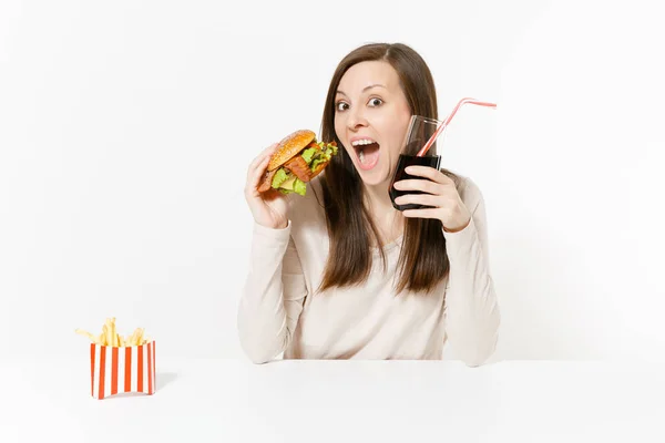 Felice divertimento giovane donna seduta a tavola con hamburger, patatine fritte, cola in bottiglia di vetro isolata su sfondo bianco. Una corretta alimentazione o un fast food classico americano. Area pubblicitaria con spazio di copia . — Foto Stock