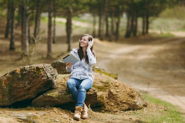 Young relaxing smiling woman in casual clothes sitting on stone