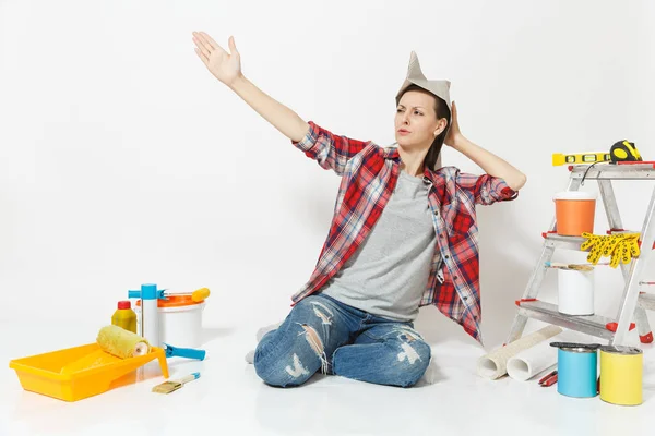 Mujer divertida feliz en sombrero de periódico sentado en el suelo con instrumentos para la renovación habitación del apartamento aislado sobre fondo blanco. Fondos de pantalla, accesorios para pegar, herramientas de pintura. Reparación concepto hogar . — Foto de Stock