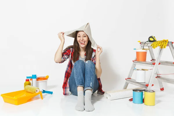 Όμορφη διασκέδαση γυναίκα στην εφημερίδα καπέλο κάθεται στο πάτωμα με τα όργανα για δωμάτιο διαμέρισμα ανακαίνιση που απομονώνονται σε λευκό φόντο. Ταπετσαρία, κόλλημα αξεσουάρ, εργαλεία βαφής. Επισκευή concept home. — Φωτογραφία Αρχείου
