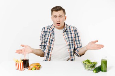 Adam masada yeşil Detoks smoothies, cam kase, salatalık, burger, patates, kola cam beyaz arka plan üzerinde izole salata ile oturuyor. Doğru beslenme, sağlıklı yaşam, lokanta, kavramı.