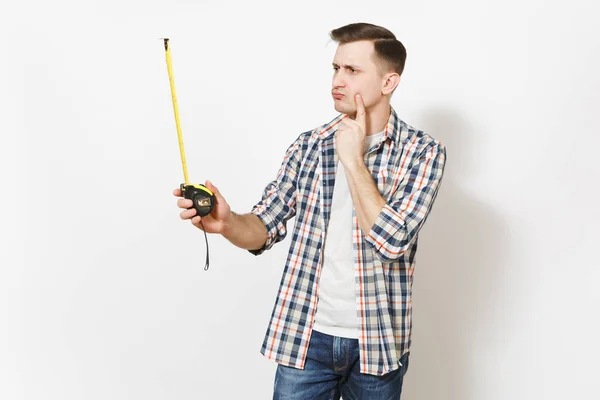 Jovem preocupado homem bonito em roupas casuais segurando fita métrica e mantendo o dedo indicador perto do rosto isolado em fundo branco. Instrumentos para renovação apartamento quarto. Reparação home concept . — Fotografia de Stock