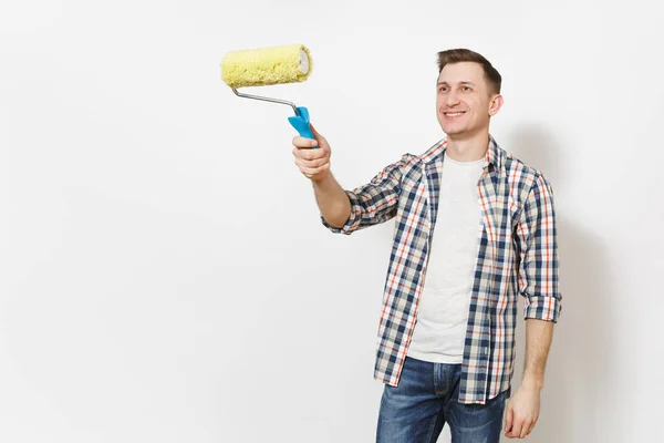 Joven hombre guapo sonriente en ropa casual apuntando rodillo de pintura para la pintura de pared en el espacio de copia aislado sobre fondo blanco. Instrumentos, herramientas para la renovación de la habitación del apartamento. Reparación concepto hogar . — Foto de Stock