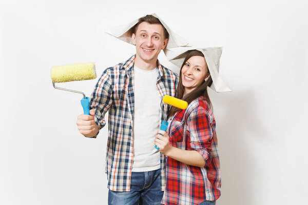 Young happy woman, man in casual clothes holding paint rollers for wall painting. Couple isolated on white background. Instruments, accessories for renovation apartment room. Repair home concept.