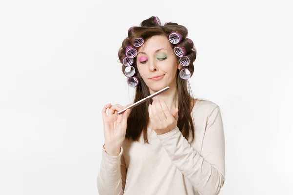 Fun young woman with curlers correcting fingernail using nail fail isolated on white background. Crazy makeup with set facial decorative cosmetics. Beauty fashion lifestyle concept. Area copy space. — Stock Photo, Image