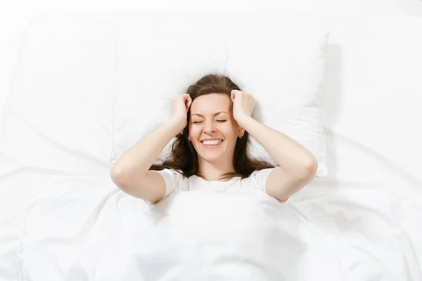 Top view of head of happy brunette young woman lying in bed with white sheet, pillow, blanket. Smiling pretty female spending time in room. Rest, relax, good mood concept. Copy space for advertisement — Stock Photo, Image