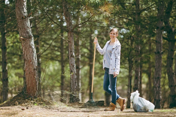 Joven sonrisa hermosa mujer limpieza y uso de rastrillo para la bolsa de basura — Foto de Stock