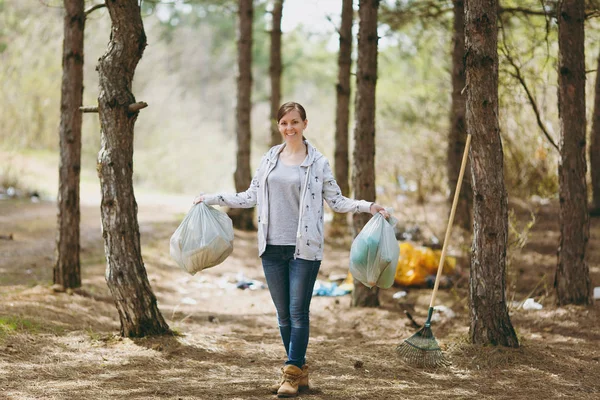 Young smiling woman in casual clothes holding trash bags cleanin