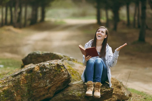 Young laughing beautiful woman sitting on stone studying reading