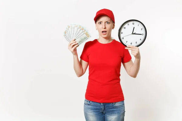 Mujer de parto en uniforme rojo aislado sobre fondo blanco. Mujer impactada en gorra, camiseta, jeans trabajando como mensajero o traficante, sosteniendo un paquete de dólares en efectivo reloj de dinero. Copiar espacio para publicidad —  Fotos de Stock