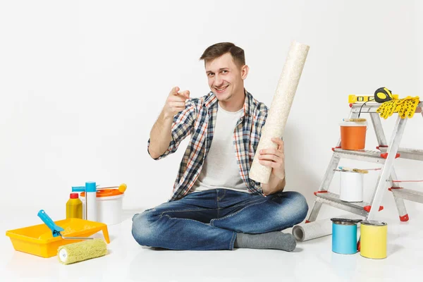 Χαμογελαστός άνθρωπος κάθεται στο πάτωμα με ρολό ταπετσαρία, casual ρούχα μέσα για ανακαίνιση διαμέρισμα δωμάτιο που απομονώνονται σε λευκό φόντο. Κόλλημα αξεσουάρ, εργαλεία βαφής. Επισκευή concept home. — Φωτογραφία Αρχείου