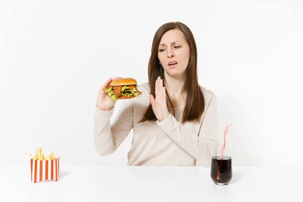 Súlyos nő látható stop gesztus asztalnál hamburger hasábburgonyával cola elszigetelt fehér background üvegben. Megfelelő táplálkozás, vagy a klasszikus amerikai gyorsétterem. Hirdetés terület másol hely. — Stock Fotó