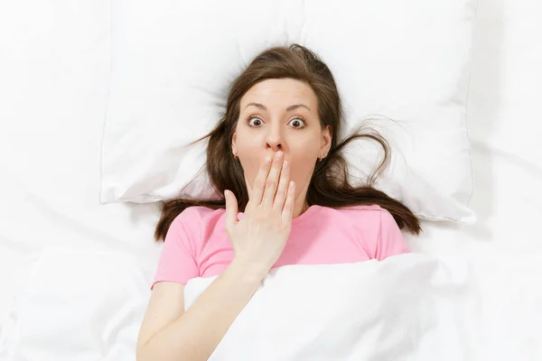 Top view of happy brunette young woman lying in bed with white sheet, pillow, blanket. Female spending time in room, cover mouth with hand. Rest, relax, good mood concept. Copy space for advertisement — Stock Photo, Image