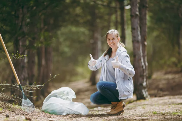 Joven mujer sonriente limpiando basura en bolsas de basura mostrando thu — Foto de Stock