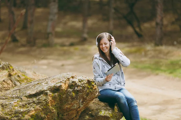 Young smiling woman in casual clothes sitting on stone listening