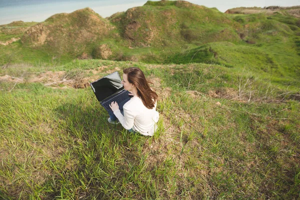 Joven mujer de negocios o estudiante sentado en la hierba usando el ordenador portátil wi — Foto de Stock