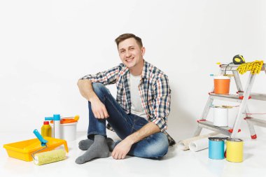 Beyaz arka plan üzerinde izole yenileme daire oda için aygıtlar ile katta oturan rahat kıyafetler içinde gülümseyen mutlu adam. , Duvar kağıdı yapıştırma aksesuarları, boyama araçlarını. Onarım ev concept.