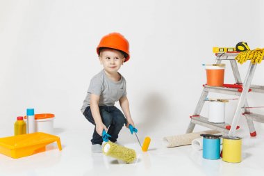 Beyaz arka plan üzerinde izole yenileme daire için aygıtlar ile turuncu koruyucu kask içinde küçük bir çocuk. , Duvar kağıdı yapıştırma aksesuarları, boyama araçlarını. Onarım ev. Ebeveynlik, çocukluk kavramı