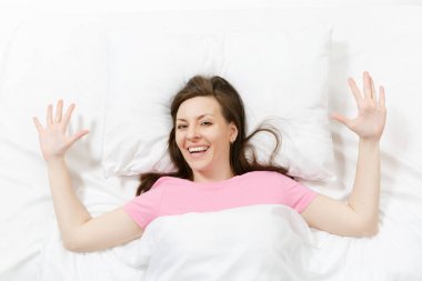 Üstten Görünüm mutlu esmer genç kadının beyaz çarşaf, yastık, battaniye ile yatakta yalan. Yayilim eller odasında vakit, gülümseyen. Dinlenmek, sakin ol, iyi bir ruh hali kavramı. Kopyalama alanı reklam.