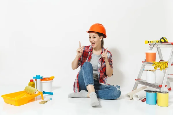 Γυναίκα στο πορτοκαλί προστατευτικό κράνος που κάθεται στο πάτωμα με τα όργανα για δωμάτιο διαμέρισμα ανακαίνιση που απομονώνονται σε λευκό φόντο. Ταπετσαρία, αξεσουάρ για την κόλληση, εργαλεία ζωγραφικής. Επισκευή concept home. — Φωτογραφία Αρχείου