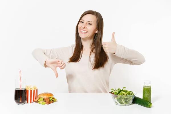 Vrouw toont duimen omhoog omlaag met groene detox smoothies, salade met glazen kom, komkommer Hamburger cola in fles geïsoleerd op een witte achtergrond. Goede voeding, gezonde levensstijl, fastfood, keuze concept. — Stockfoto