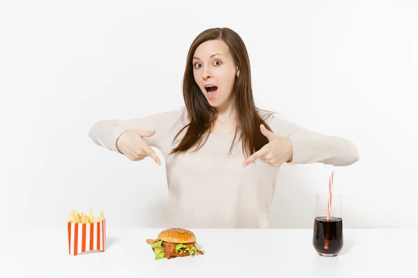 Vacker ung kvinna sitter vid bord med hamburgare, pommes frites, cola i glasflaska isolerade på vit bakgrund. Rätt kost eller amerikansk klassisk snabbmat. Reklam med kopia utrymme. — Stockfoto