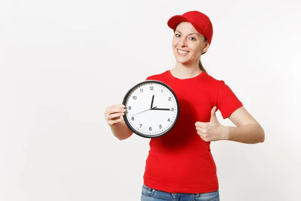 Livraison femme en uniforme rouge isolé sur fond blanc. Femme professionnelle en bonnet, t-shirt, jeans travaillant comme coursier ou revendeur, tenant l'horloge ronde, montrant dans le temps. Espace de copie pour la publicité . — Photo