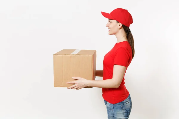 Mulher de entrega em uniforme vermelho isolado no fundo branco. Feminino em boné, camiseta, jeans trabalhando como mensageiro ou revendedor segurando caixa de papelão. A receber o pacote. Espaço de cópia para propaganda. Vista lateral — Fotografia de Stock