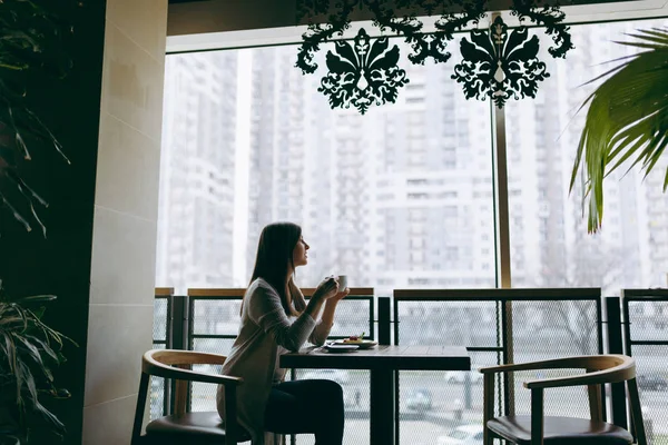 Atrakcyjna młoda kobieta siedzi sama w pobliżu duże okno w s kawy — Zdjęcie stockowe