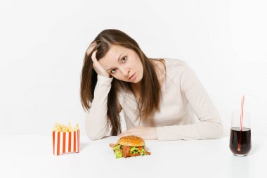 Üzgün yorgun kadın masada oturan hamburger, patates kızartması, cam şişede cola ile baş el koymak beyaz arka plan üzerinde izole. Doğru beslenme veya Amerikan Klasik fast food. Kopya alanı alanı
