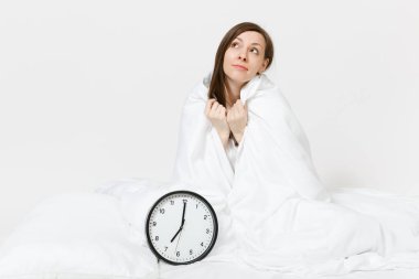 Genç kadın yatakta oturuyordu yuvarlak saat, beyaz çarşaf, yastık, battaniye beyaz arka plan üzerinde kaydırma ile. Güzellik kadın uyanmak erken sabah, odasında vakit. Dinlenme, iyi ruh kavramı