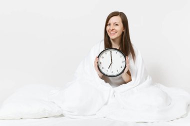 Genç kadın yatakta oturuyordu yuvarlak saat, beyaz çarşaf, yastık, battaniye beyaz arka plan üzerinde kaydırma ile. Güzellik kadın uyanmak erken sabah, odasında vakit. Dinlenme, iyi ruh kavramı