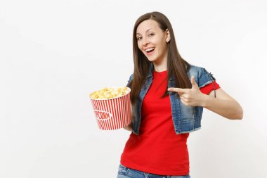 Film film izlerken, işaret parmağı Kova patlamış mısır beyaz arka plan üzerinde izole üzerinde tutarak rahat kıyafetler içinde genç gülümseyen güzel esmer kadın portresi. Sinema kavramı duygular