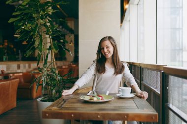 Yalnız büyük kahve dükkanında tablo penceresinde yakınındaki kapuçino, bardak ile oturan kadın kek, restoranda serbest zaman sırasında rahatlatıcı. Pc tablet bilgisayar dinlenme kafede çalışan erkek. Yaşam tarzı kavramı