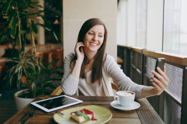 Fincan kapuçino, kafede oturan kadın cep telefonunda selfie yapıyor, restoranda serbest zaman sırasında rahatlatıcı kek. Tablet bilgisayar dinlenme kafede çalışan erkek. Yaşam tarzı kavramı