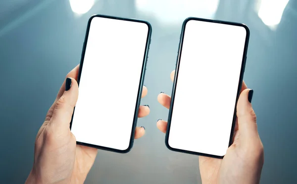 女性の手側に2つのスマートフォンを保持する。コンセプト- 2つの製品またはサービスを比較、分析、または一致させます。清潔でぼやけた現代の背景。コピースペースのある空白の画面-画像 ストック写真